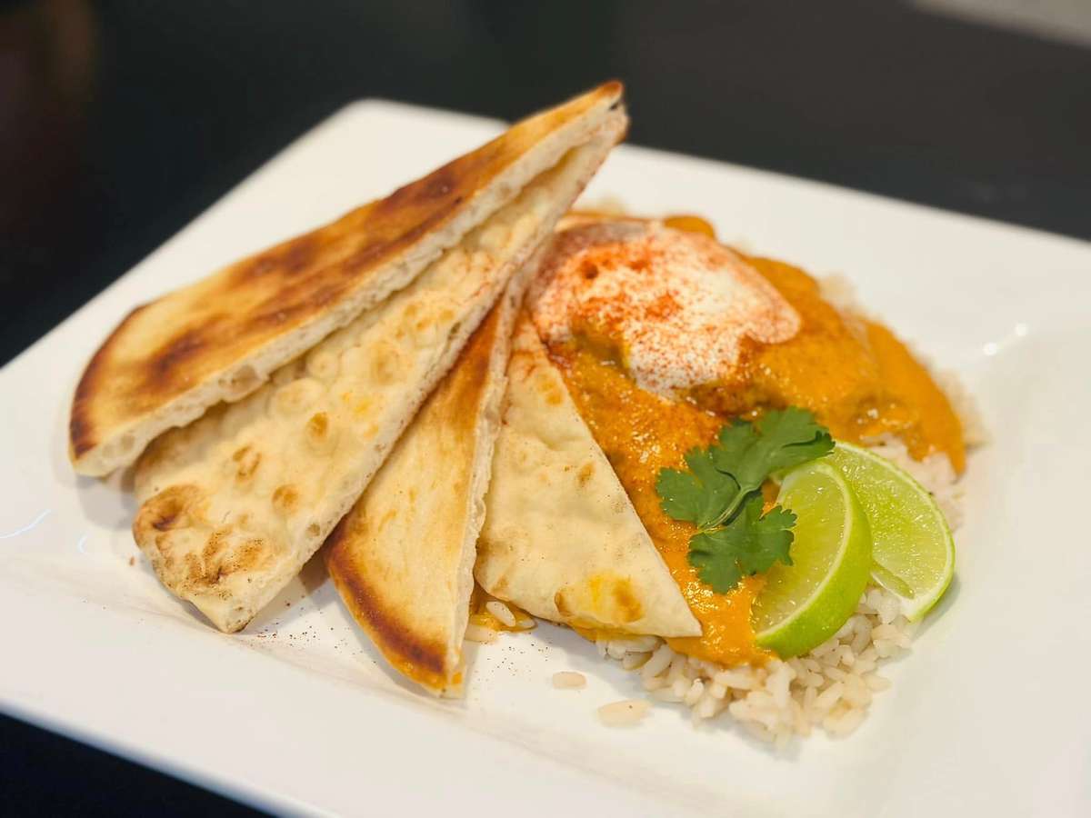 A plate of naan bread with rice, chicken curry, topped with sour cream, cilantro, lime wedges, and sprinkled with paprika.