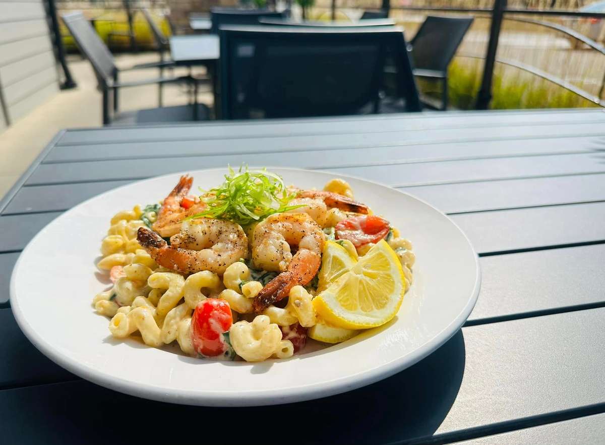 Shrimp pasta with creamy sauce, served with a slice of lemon and garnished with green onions. The dish is placed outdoors on a sunny day.
