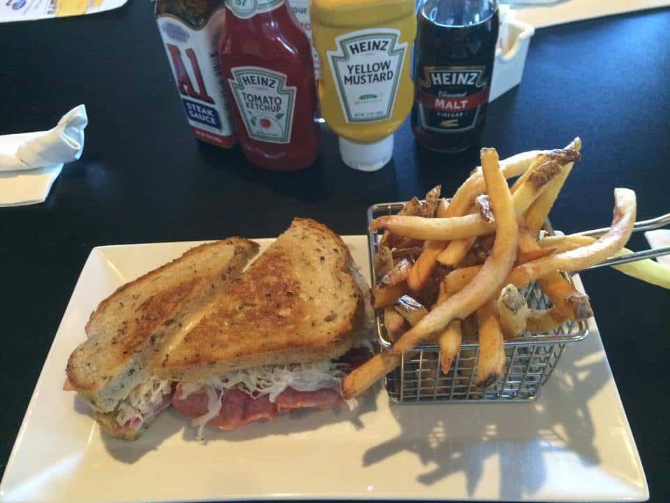 NY reuben on a plate with fries and assorted condiments