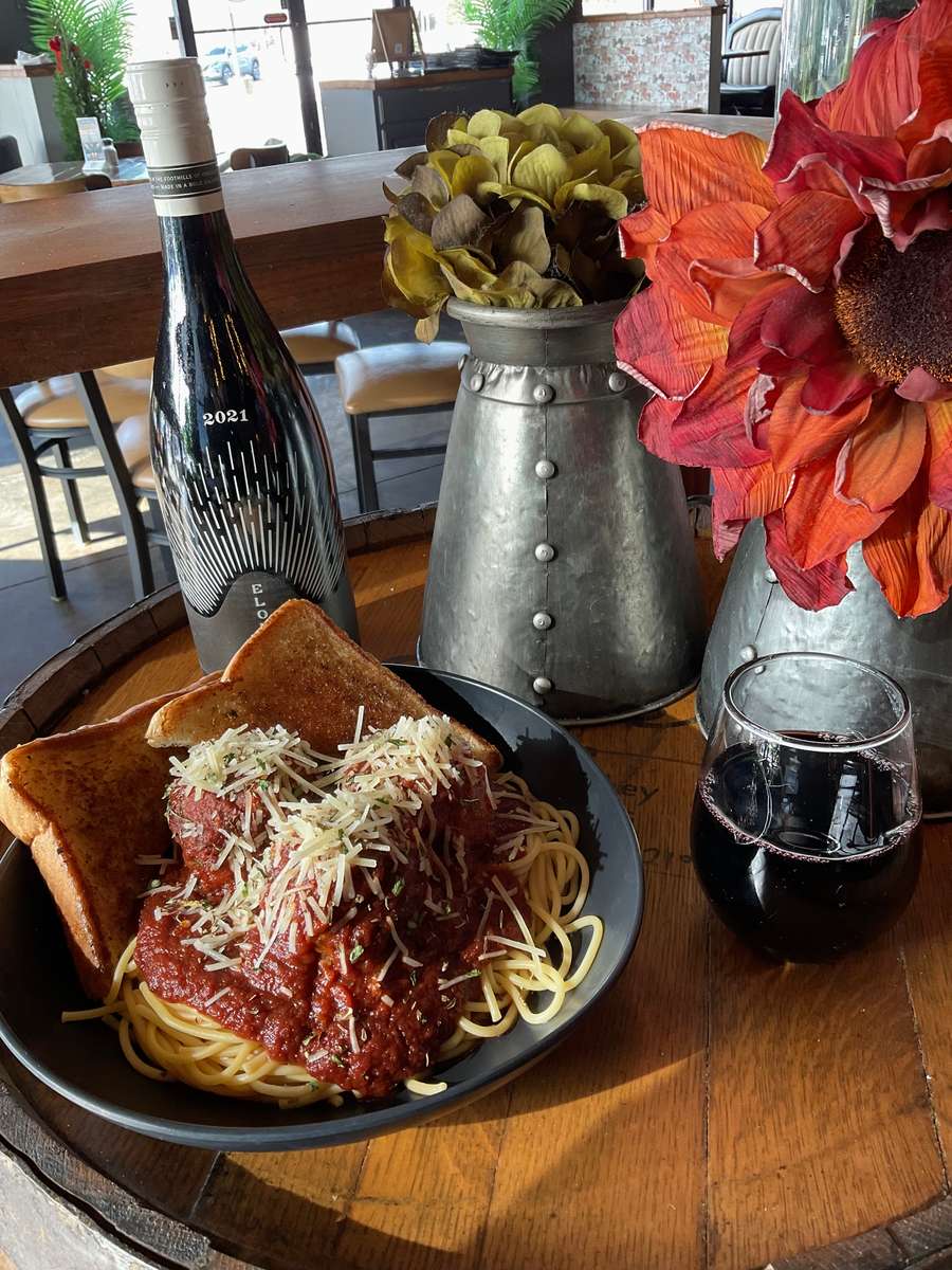 Spaghetti and meatballs topped with marinara sauce and grated cheese, served with toasted bread and red wine on a wooden table.