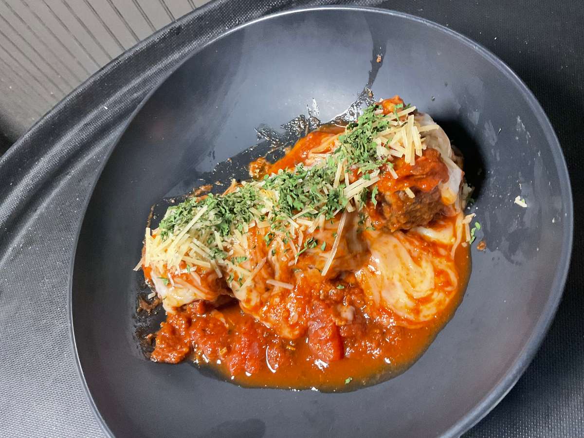 Stuffed cabbage rolls topped with rich tomato sauce, grated cheese, and fresh herbs served in a black bowl.