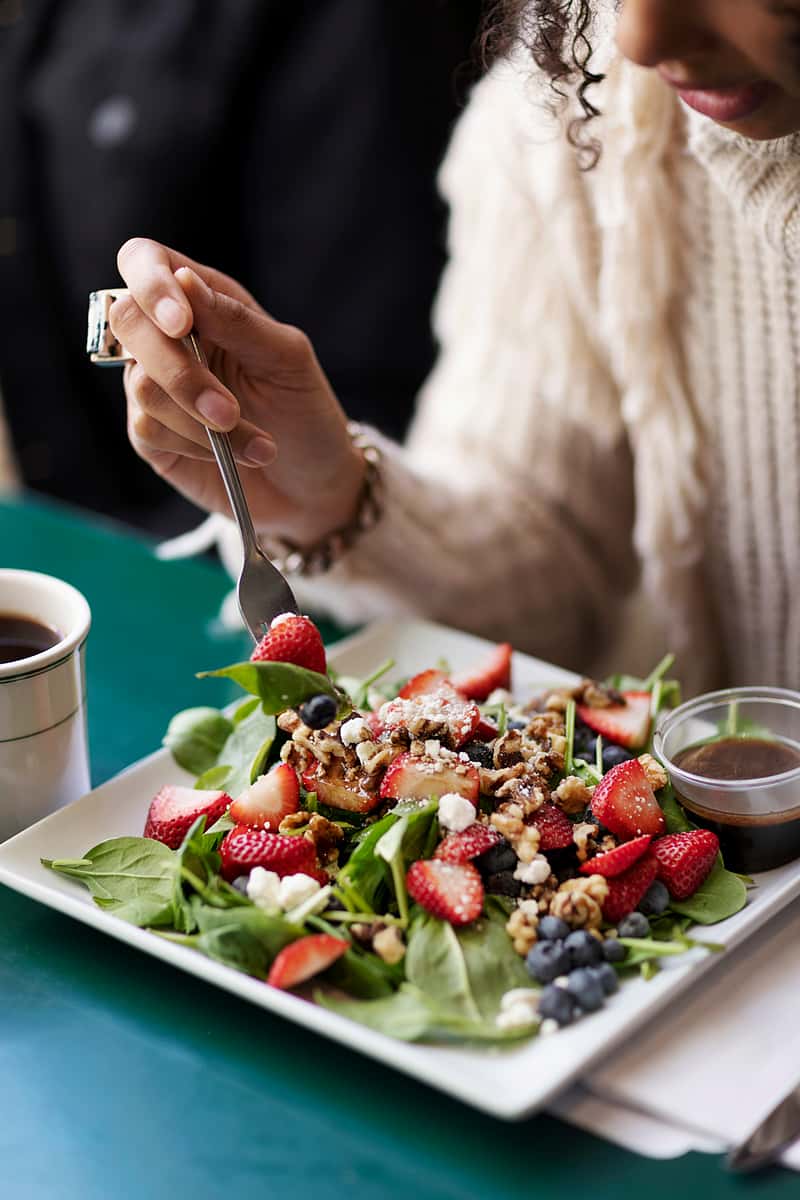 A fresh spinach salad topped with strawberries, blueberries, granola, and feta cheese, accompanied by a small container of dressing.