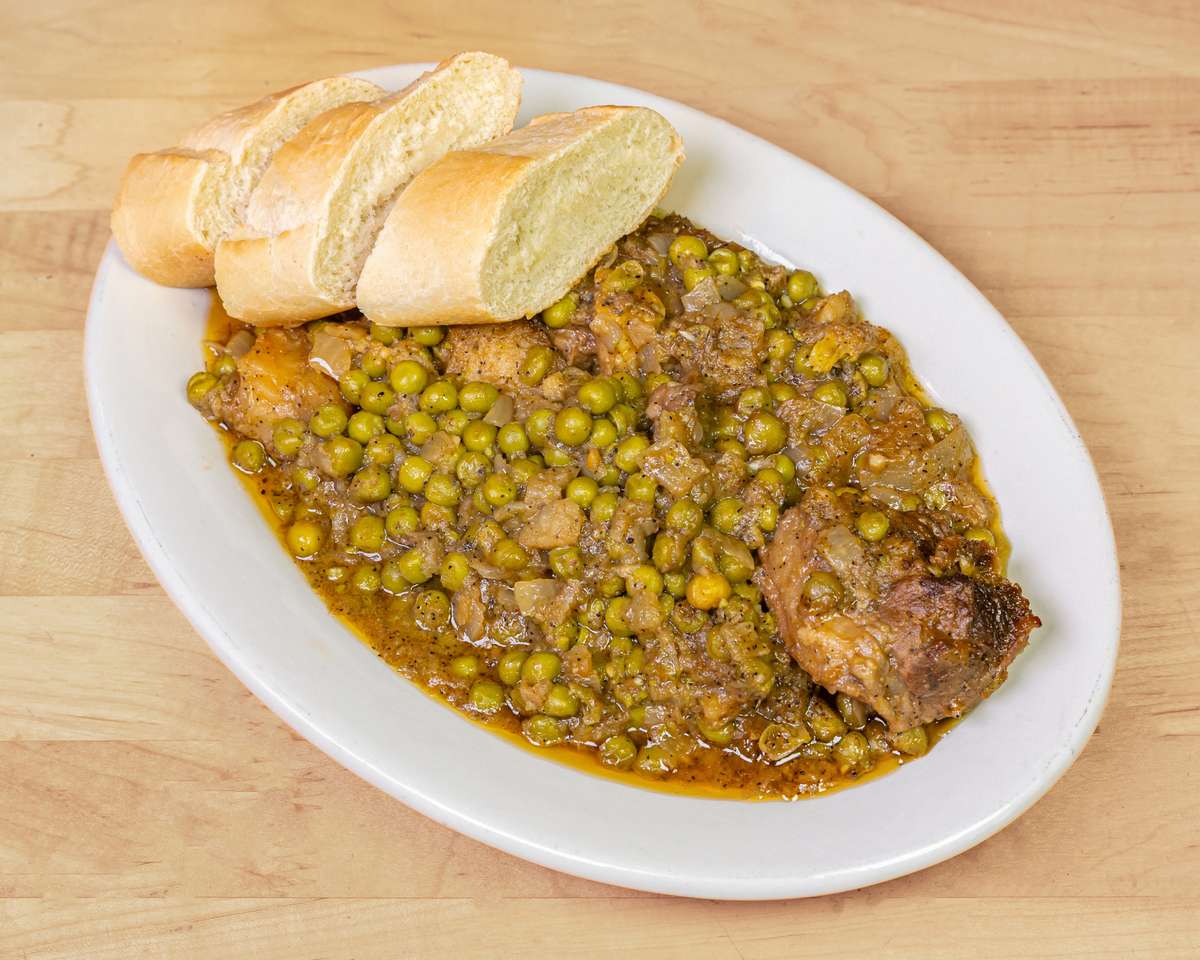 West African-style green pea and chicken stew simmered with onions and spices, served with slices of crusty French bread on a white plate.
