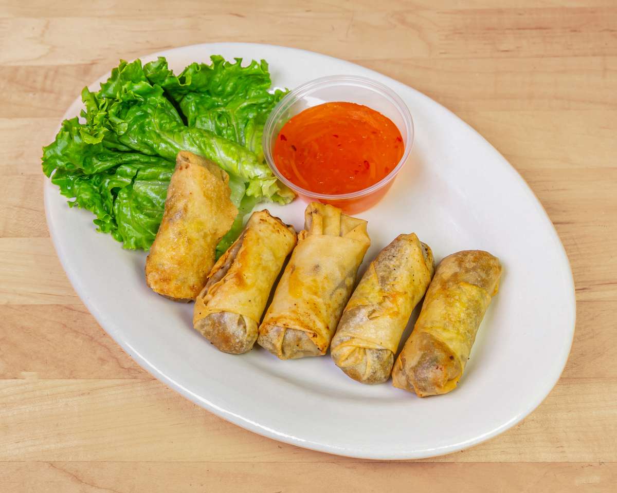 Plate of crispy beef spring rolls served with fresh romaine lettuce and a side of sweet chili dipping sauce, offering a crunchy appetizer popular in West African and fusion cuisines.