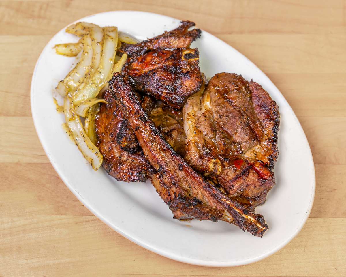 Plate of flame-grilled goat meat and ribs seasoned with West African spices, served with sautéed onions, highlighting a bold and smoky Nigerian-style barbecue dish.