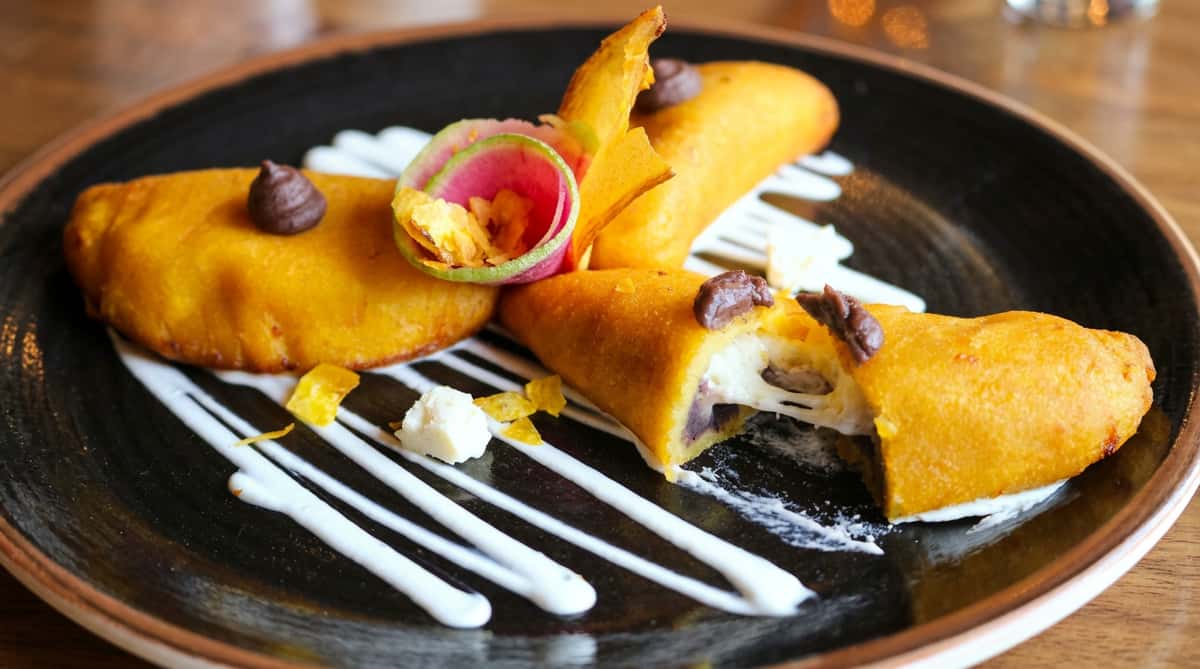 Crispy sweet plantain empanadas filled with melted cheese and black beans, garnished with crema and fresh edible flowers at Hugo's restaurant.