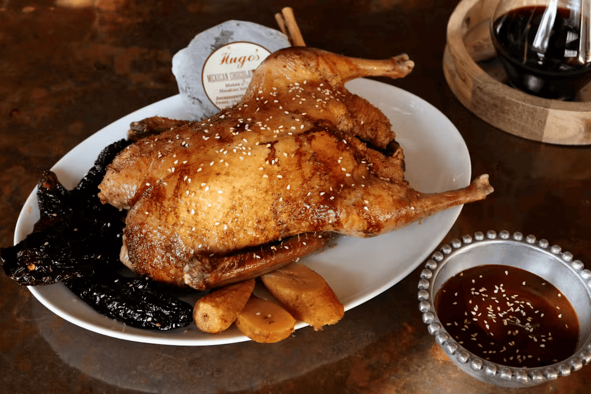 Roasted duck with rich mole poblano sauce, served with seasonal sides at Hugo's upscale Mexican restaurant.