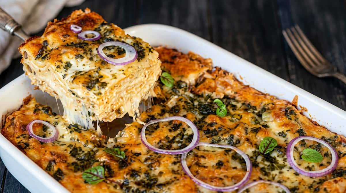Cheesy pesto bread with red onion rings, being lifted from a white baking dish.