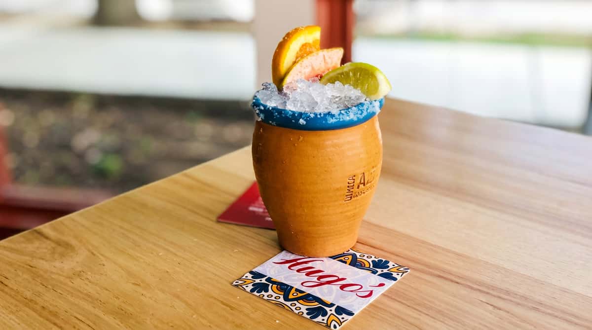 Clay cup with blue rim, filled with crushed ice, an orange slice, a grapefruit slice, and a lime wedge.