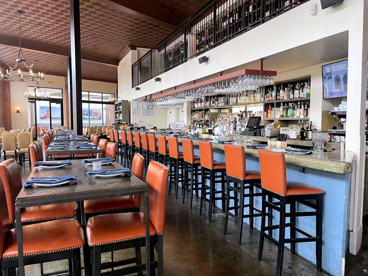 Long bar area at Hugo's restaurant featuring orange bar stools, full-service bar, and an inviting upscale dining atmosphere.