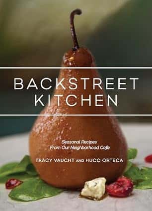 Backstreet Kitchen cookbook standing beside a handcrafted cocktail garnished with a cherry on a rustic wooden table.