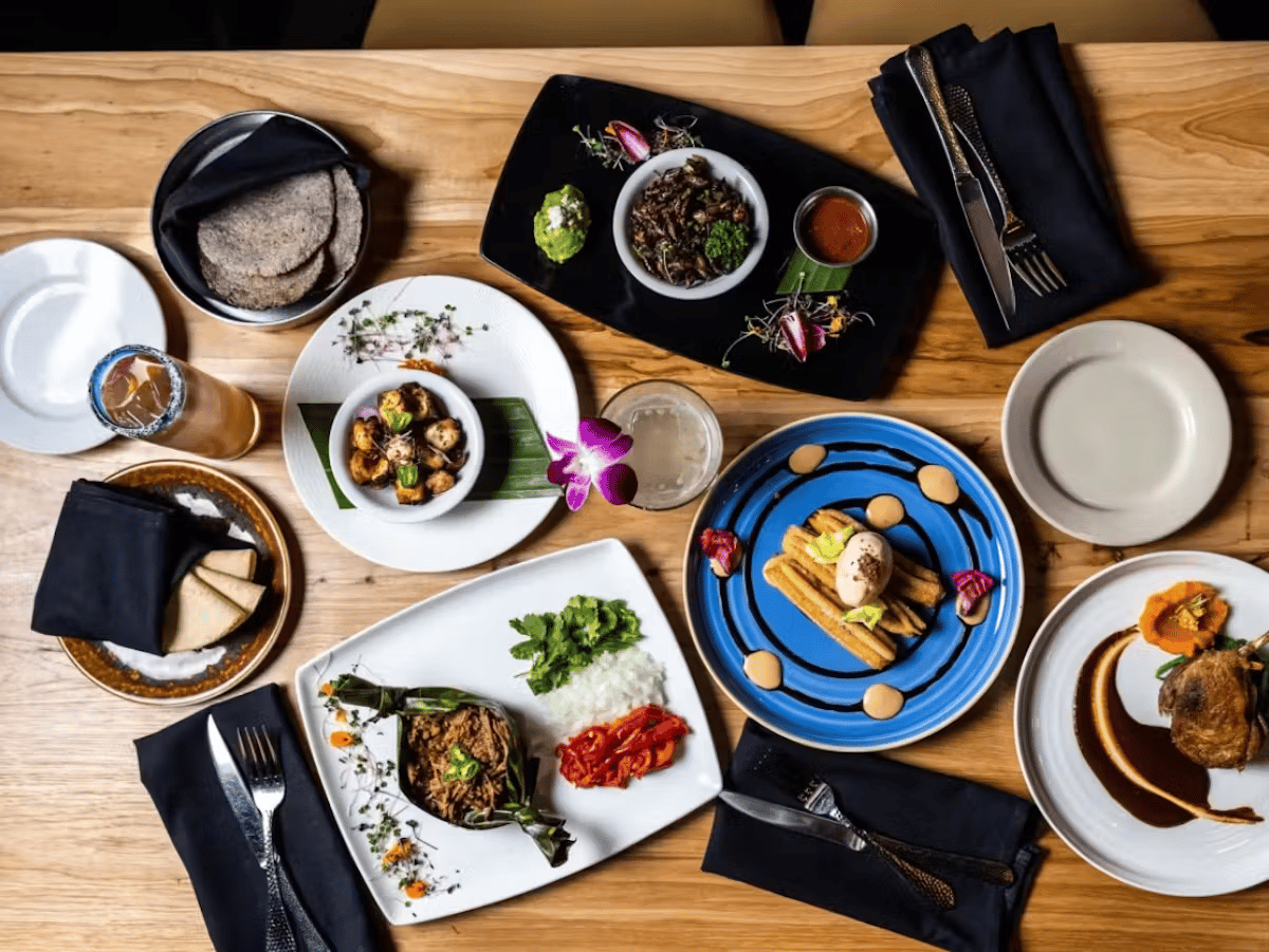 Overhead view of Hugo's signature Mexican dishes and cocktails served family-style on a wooden table.