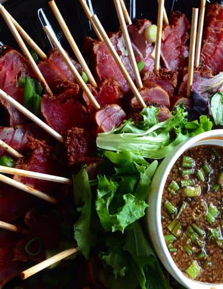 catering display of tuna on skewers topped with greens and sauce on the side