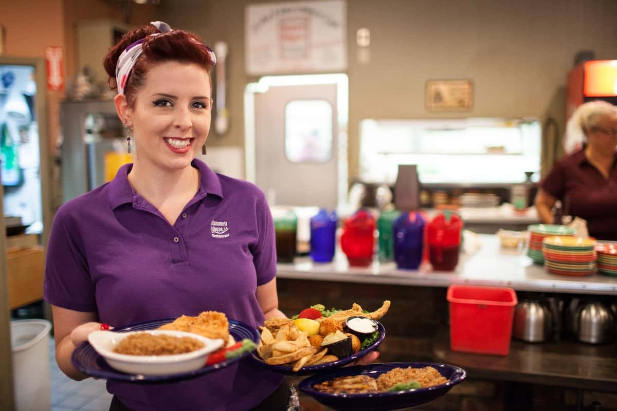 waitress smiling at the camera holding various dinner dishes