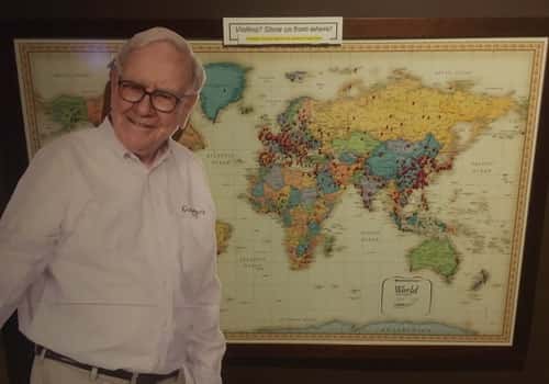 Warren Buffett standing beside the Gorat's Steak House world map, highlighting the iconic Omaha restaurant's long-standing tradition and loyal visitors.