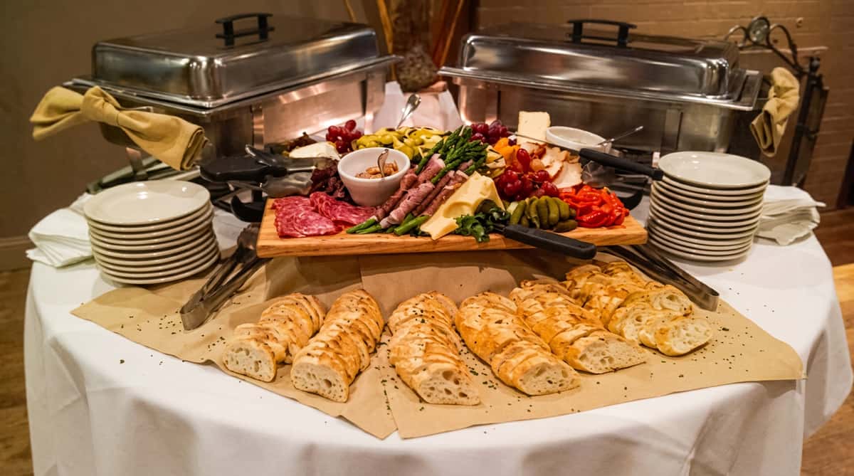 A buffet table with a charcuterie board of meats, cheeses, grapes, vegetables, and baguettes.