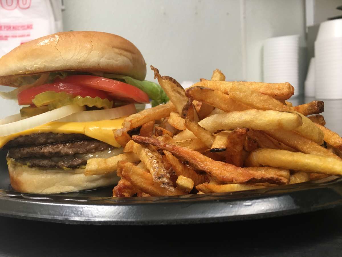 Cheeseburger stacked with three beef patties, cheddar, onions, pickles, lettuce, and tomato, served with a generous side of fries.