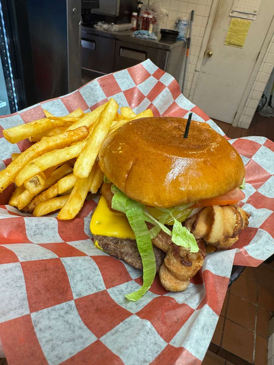A large cheeseburger with two beef patties, melted cheese, lettuce, and onions, served with crinkle-cut fries in a basket.