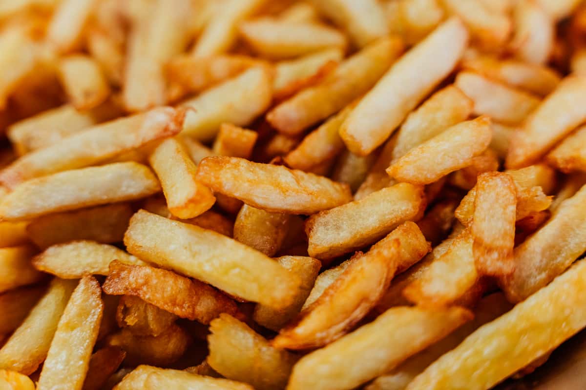 A close-up view of golden, crispy French fries stacked together, with a focus on their uneven edges and golden-brown texture.