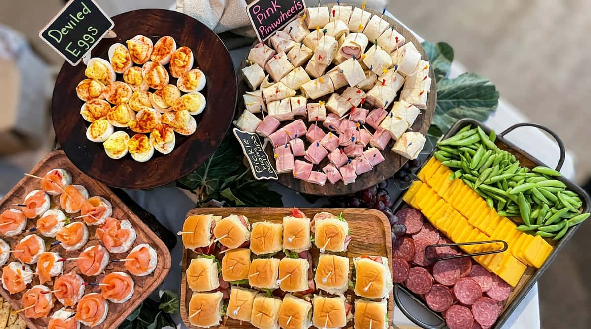A buffet display of deviled eggs, two kinds of pinwheel roll-ups, green beans, cheese, and salami.