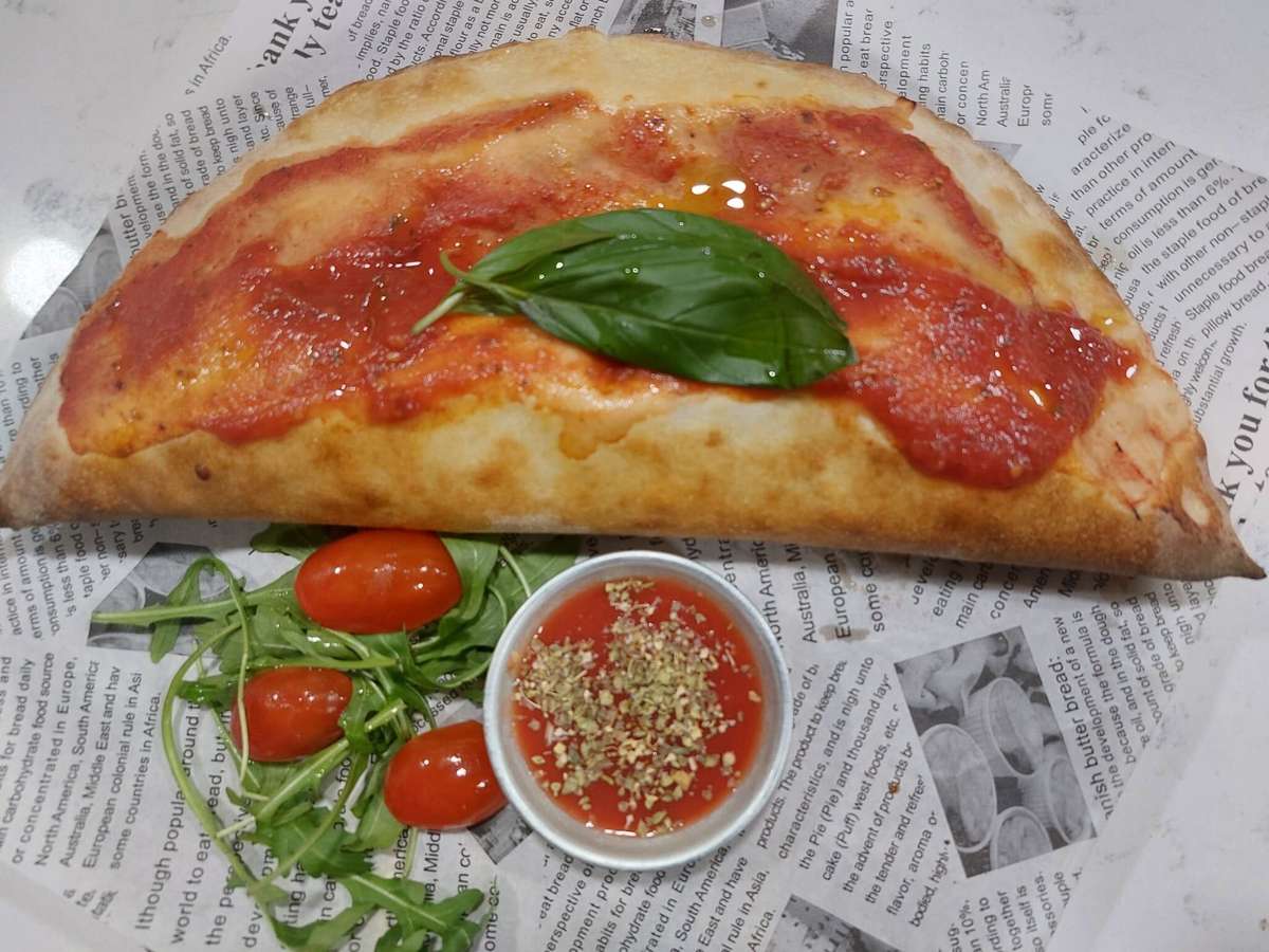 Golden-baked calzone topped with tomato sauce and fresh basil, served with marinara dip, cherry tomatoes, and arugula