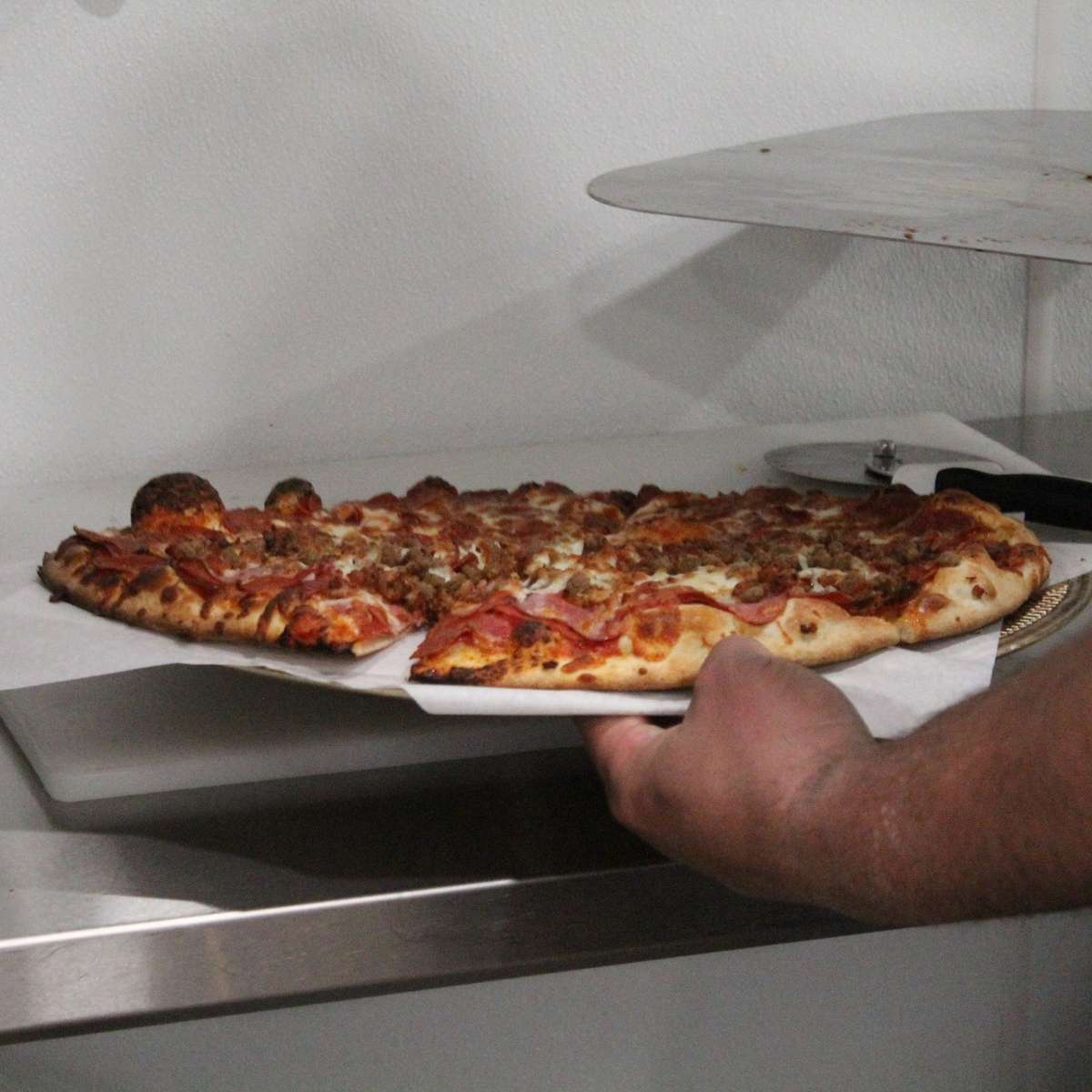 Person putting finished pizza on kitchen counter