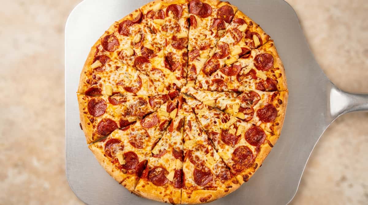 Pepperoni and pineapple pizza, cut into slices, on a metal pizza peel.
