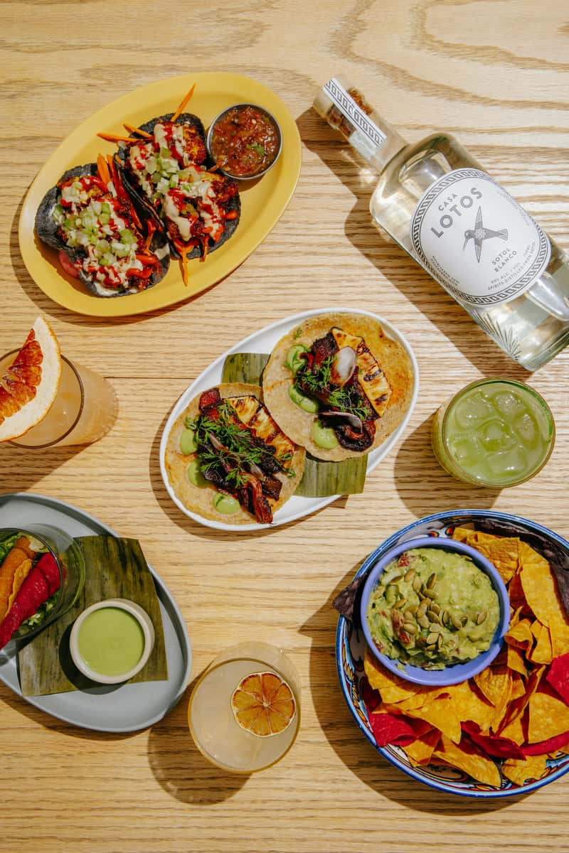 Colorful spread of tacos, chips, guacamole, and cocktails arranged on a wooden table at Jajaja Mexicana.