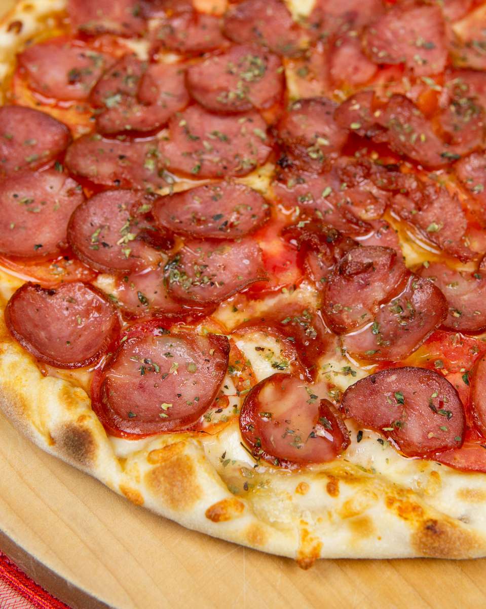 Thin-crust pepperoni pizza topped with evenly spaced sausage slices, fresh herbs, and a golden, bubbly cheese layer.