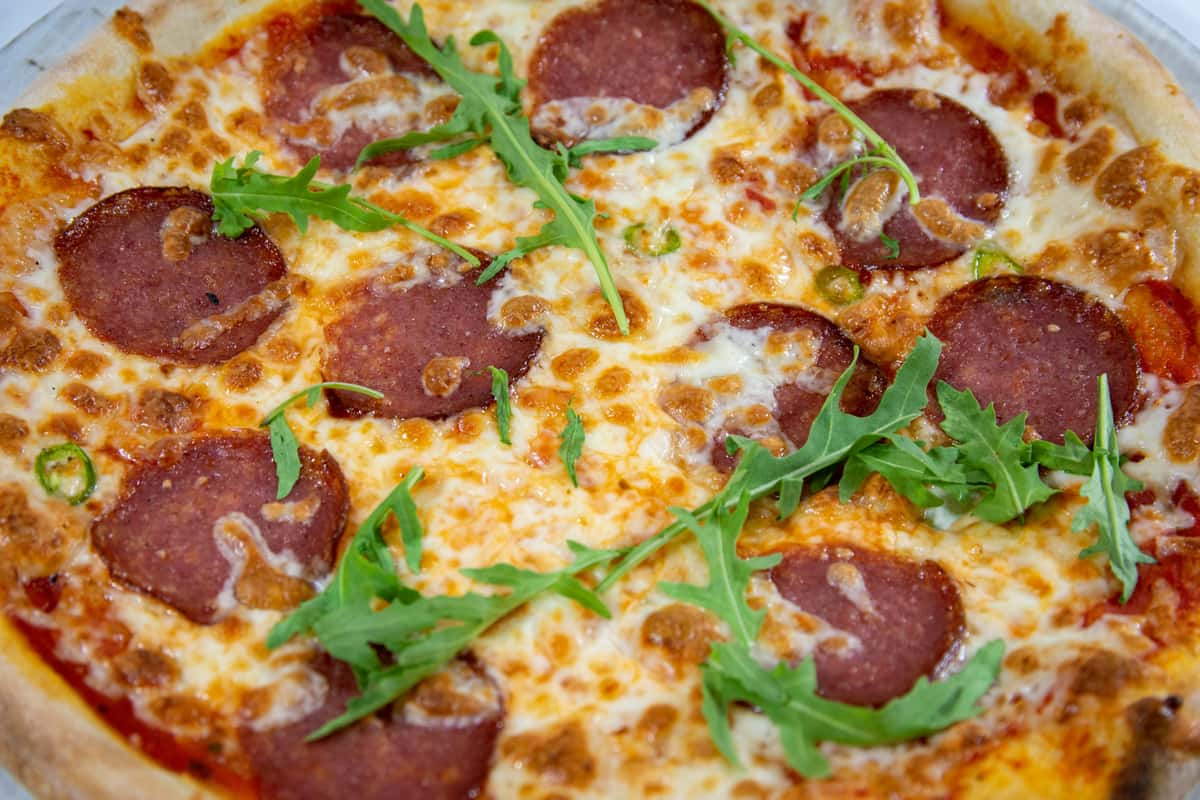Salami pizza with fresh arugula and spicy green peppers on a golden-brown crust, combining Italian flavor with a fresh twist.
