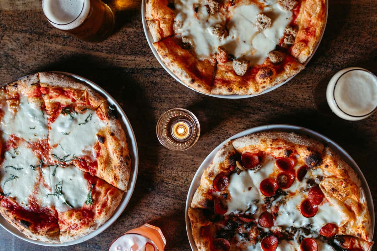 Three pizzas with various toppings on wooden table
