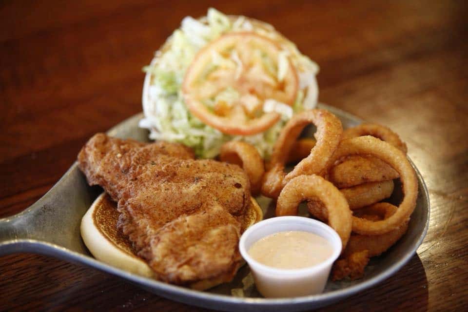 Fried fish filet with lettuce and tomato on a bun with onion rings and dipping sauce