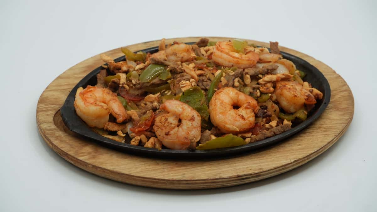Sizzling shrimp fajitas with grilled onions, bell peppers, chicken, and steak served on a hot cast iron skillet atop a wooden board—vibrant and flavorful, straight from the grill at a Mexican restaurant.