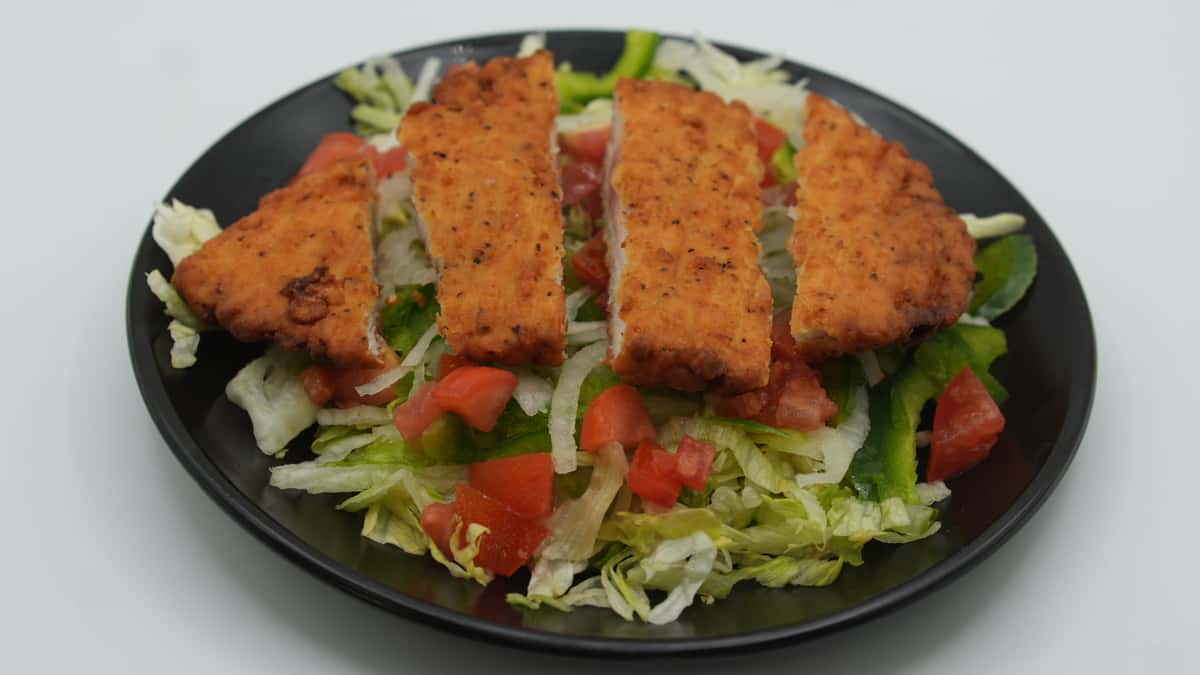 Fresh Mexican-style salad topped with crispy breaded chicken strips, served over shredded lettuce, diced tomatoes, and green bell peppers on a black plate—perfect for a lighter option at a Mexican grill.