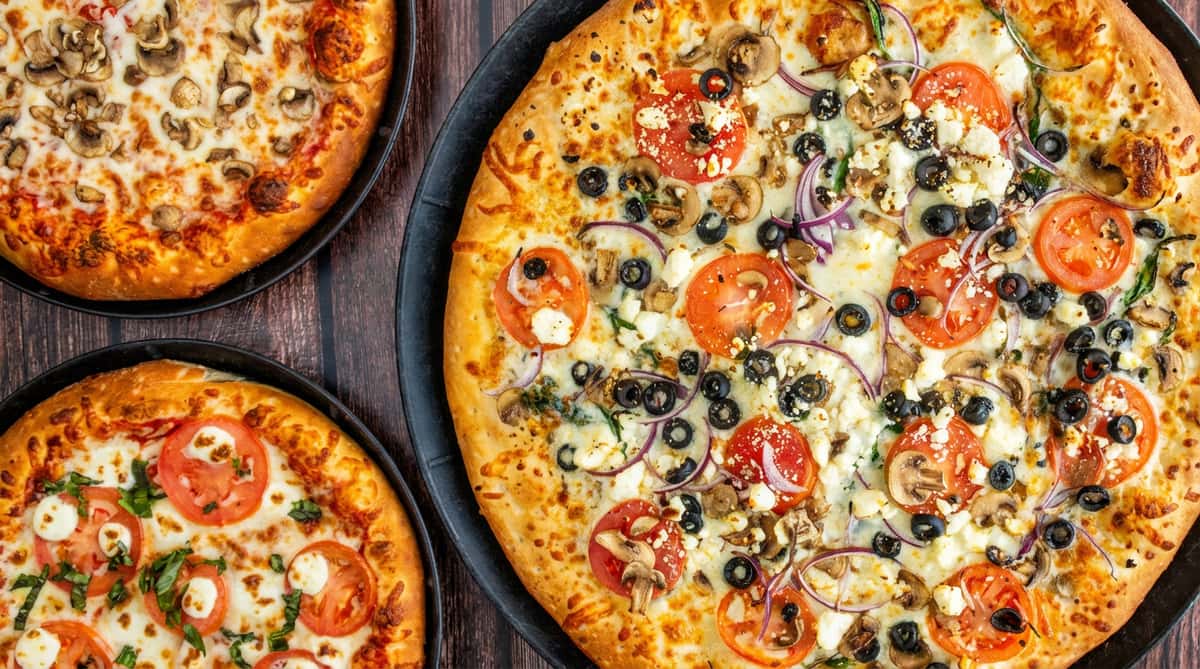 Three pizzas: two smaller with mushrooms and mozzarella, one larger with mushrooms, olives, red onion, tomatoes, and feta.