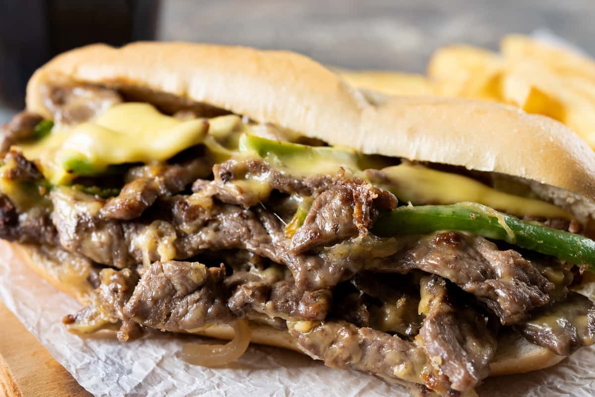 Cheesesteak featuring sliced beef, melted cheese, and vegetables, served in a hoagie bun.
