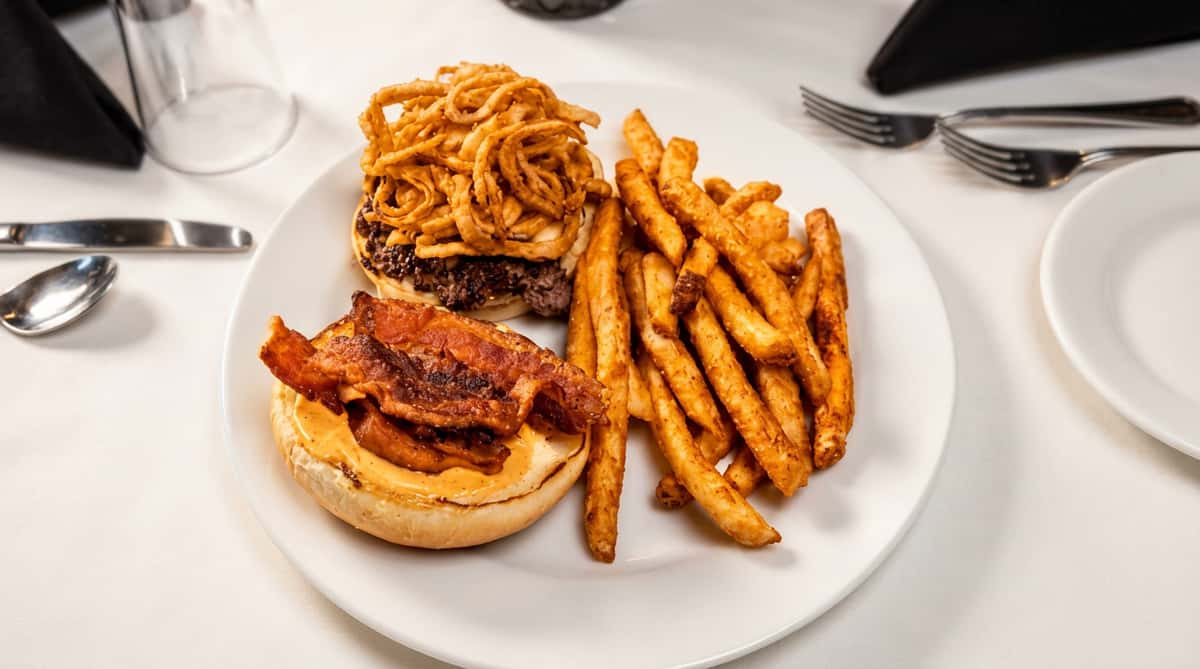 Bacon cheeseburger with crispy onion strings, an open bottom bun, and a side of golden-brown french fries.
