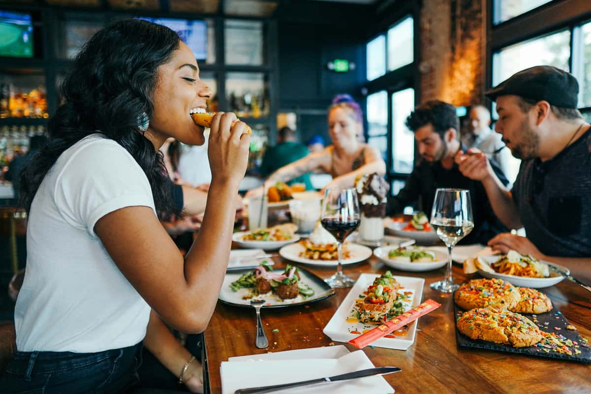 Group of friends enjoying a vibrant meal at a modern restaurant with shared plates, colorful desserts, and glasses of wine.
