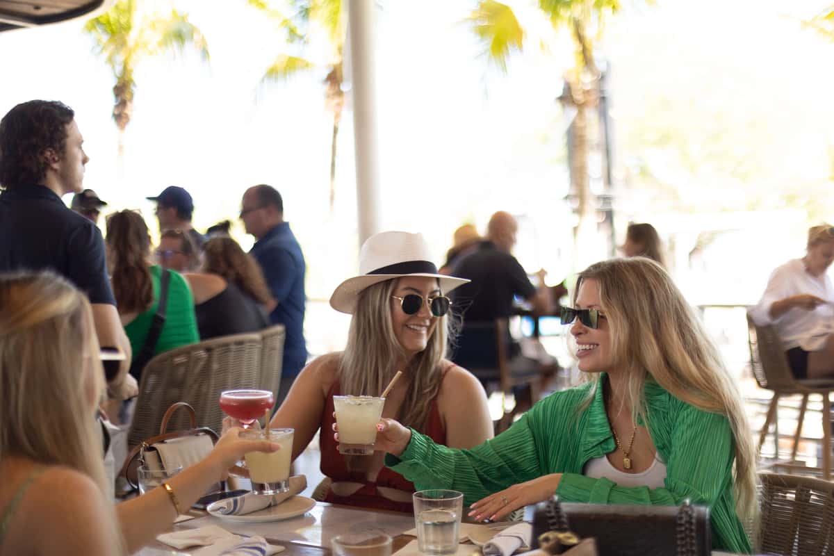 Friends toasting cocktails at a lively outdoor Miami restaurant