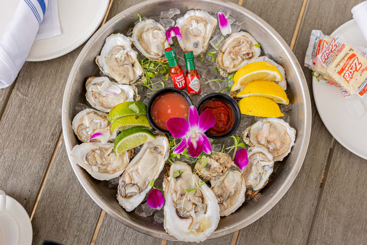 Raw oyster platter served on ice with lemon, lime, sauces, and edible flowers