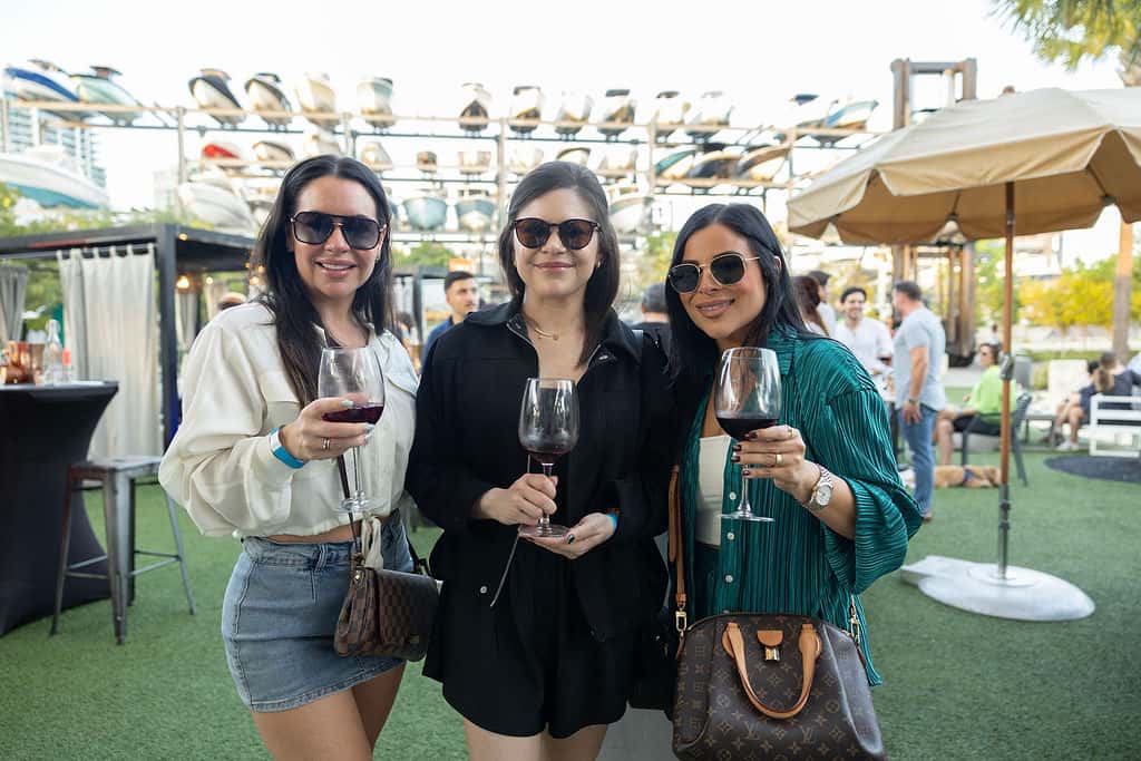 Three women holding glasses of wine at an outdoor waterfront event