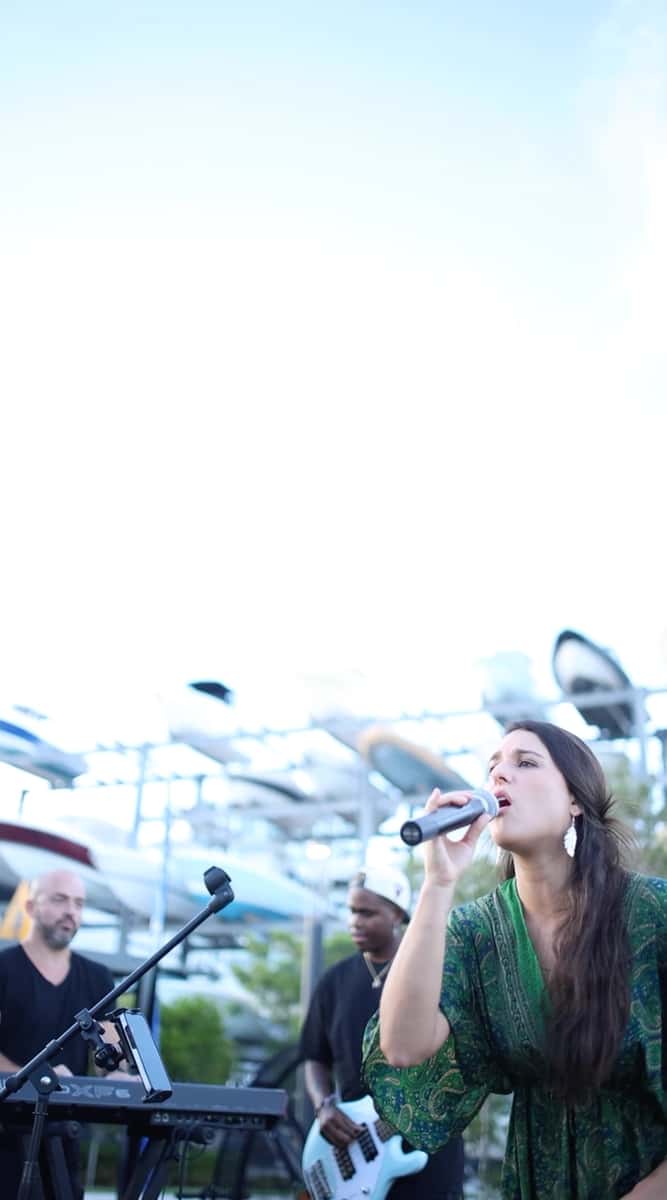 Female singer performing live with a band at an outdoor waterfront venue