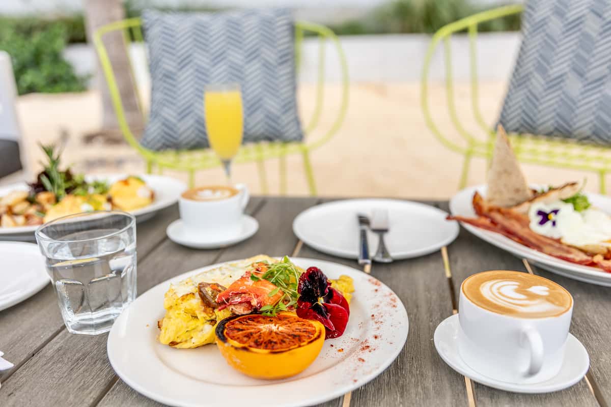 Tropical outdoor brunch spread with eggs, seafood, coffee, and colorful garnishes.