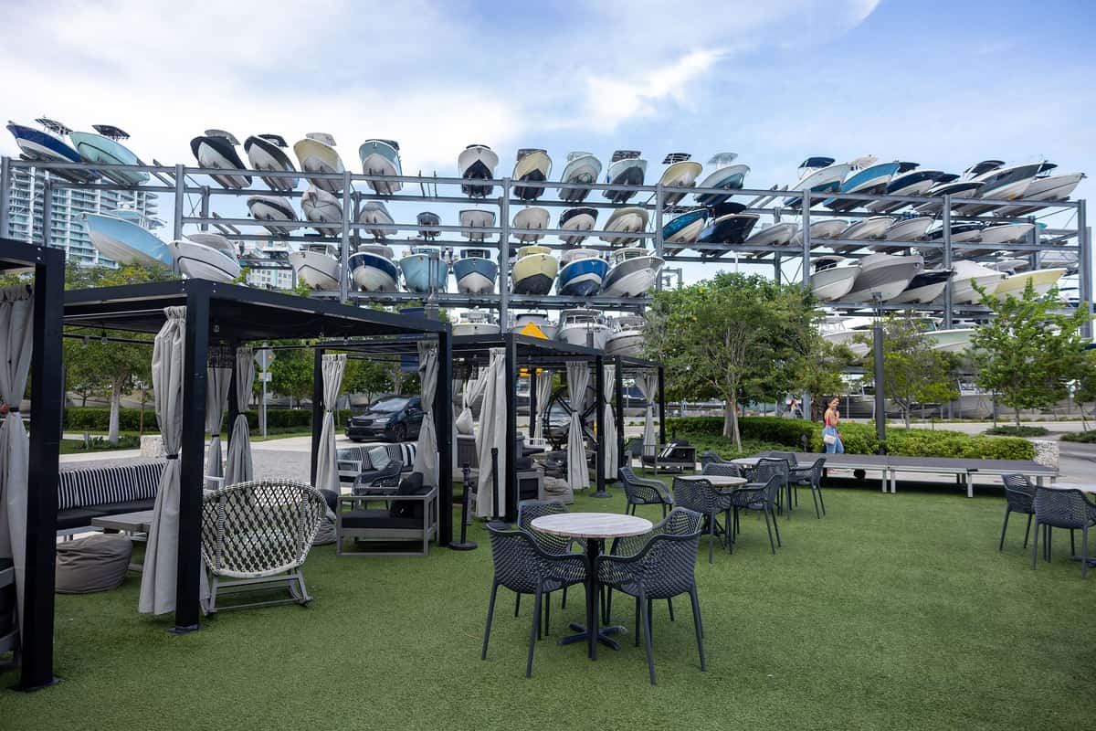 Outdoor cabanas and patio seating beside stacked boats at a Miami marina