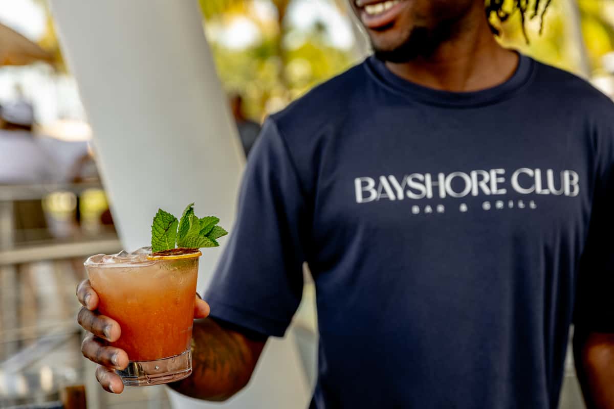 Bayshore Club staff member holding an iced cocktail garnished with mint and dried citrus.