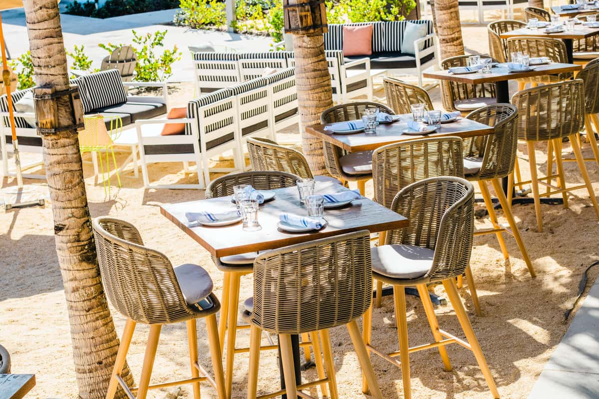 Tropical outdoor restaurant dining area with wicker chairs, wood tables, and palm trees