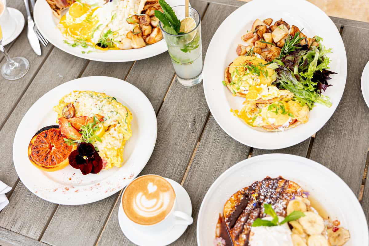Outdoor brunch spread featuring lobster eggs, French toast, coffee, and a refreshing mint cocktail.