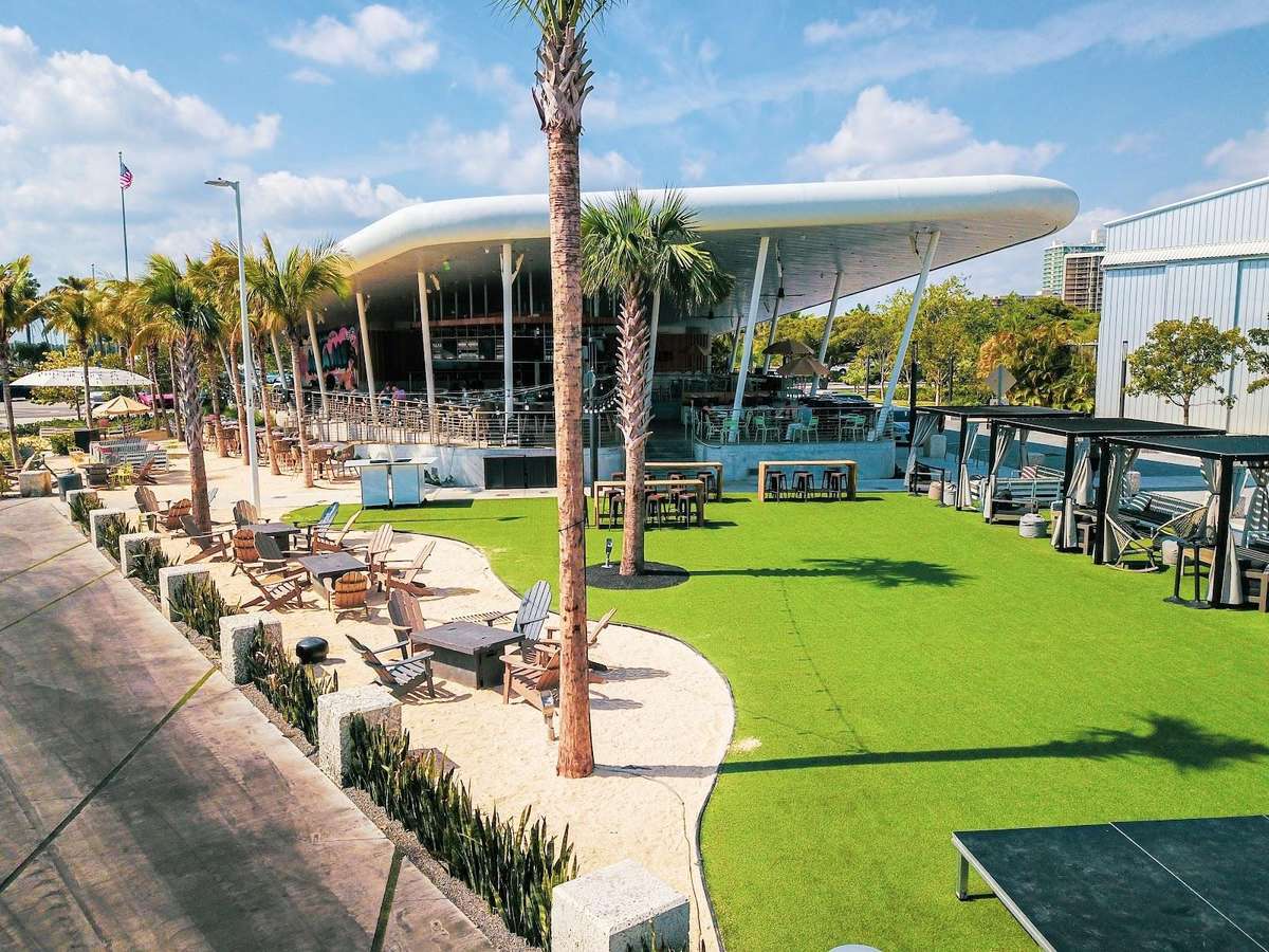 Bayshore Club outdoor lawn with cabanas, patio seating, palm trees, and waterfront views.