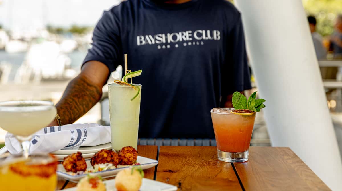Bayshore Club outdoor table with cocktails, appetizers, and a server in branded shirt