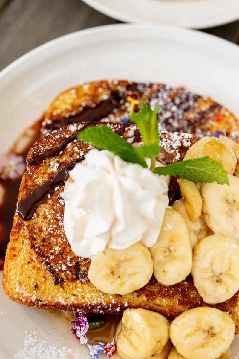 French toast topped with banana slices, chocolate sauce, whipped cream, powdered sugar, and fresh mint.